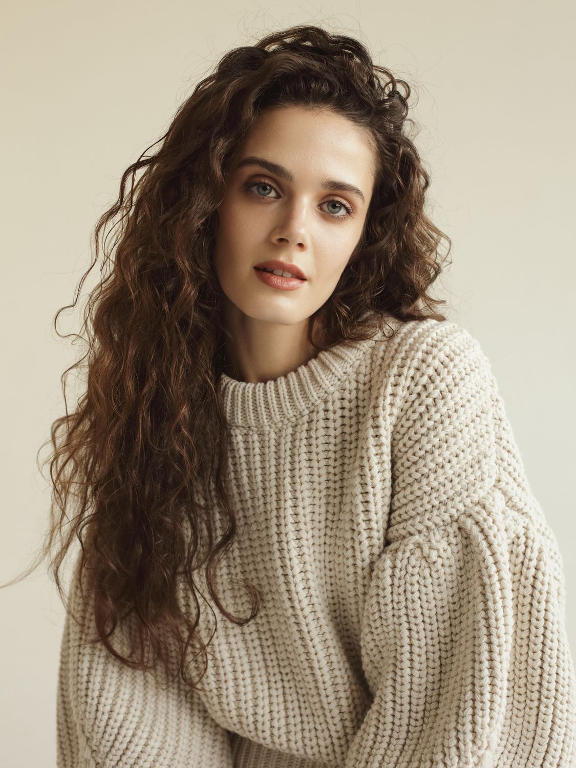 Woman with curly hair in cozy sweater.
